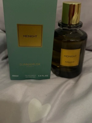Midnight parfym från Sunna Musk - Midnight från Sunna Musk är en elegant parfym i en mörkbrun glasflaska med guldfärgat lock. Flaskan rymmer 100 ml och har en stilren design med en gul etikett. Doften är Eau de Parfum endast testad