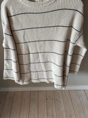 Beige stickad tröja med svarta ränder - Snygg beige stickad tröja från H&M i storlek XS. Tröjan har tunna svarta horisontella ränder, rund halsringning och avslappnad passform. Perfekt för lager på lager och enkel att matcha med jeans eller kjol.