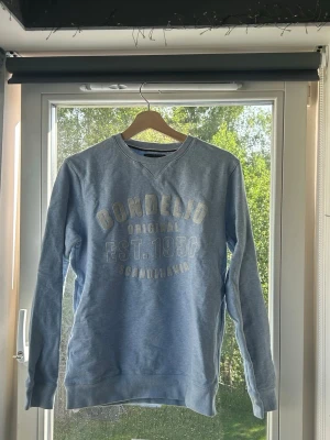 Ljusblå sweatshirt från Bondelid - Ljusblå sweatshirt från Bondelid med tryck framtill i vitt och beige. Klassisk rund halsringning och ribbade muddar vid ärmslut och nederkant. Perfekt för en avslappnad och stilren look.