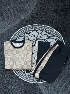 Beige LV pyjamas-set med logomönster - Snyggt pyjamas-set från Louis Vuitton i beige och svart. Tröjan har klassiskt LV-logomönster och svarta muddar vid halsen. Byxorna är svarta med beigea sidopaneler i samma logomönster. Perfekt för chillkvällar hemma och riktigt trendig look.