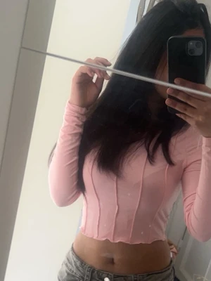 Ljusrosa croppad långärmad topp - Trendig ljusrosa croppad topp med långa ärmar och figurnära passform. Toppen har sömdetaljer framtill som ger en snygg struktur och är perfekt för att styla med höga jeans eller kjol.
