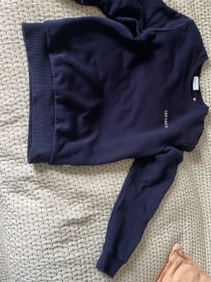 Mörkblå sweatshirt från Les Deux - Mörkblå sweatshirt från Les Deux med rund halsringning och diskret broderad logga på bröstet. Tröjan har ribbade muddar vid ärmslut och nederkant. Perfekt för en avslappnad och stilren look.