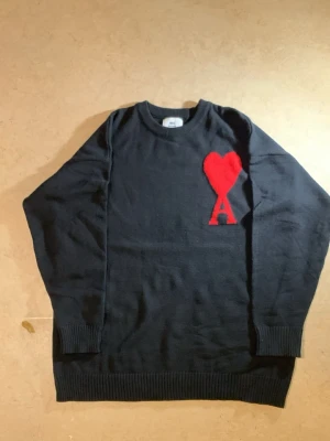 L. Tröja från Ami pari - Helt ny, jag tog på mig den bara 1 gång inga prislapp för det va present (äkta) den var för tight. Fick den som present. Min storlek är XL.”Svart stickad tröja från Ami Paris med röd hjärtlogga och bokstaven A på bröstet. Klassisk rund halsringning och ribbade muddar vid ärmslut och nederkant. Perfekt för dig som gillar stilrena plagg med en twist.