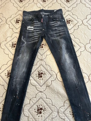 Mörkblå distressed jeans Dsquared2 - Säljer ett par mörkblå jeans från Dsquared2 med skinny fit. Jeansen har slitningar, färgstänk och patchdetaljer framtill för en riktigt edgy look. Klassisk femficksmodell med låg midja och dragkedjegylf. Perfekta för dig som gillar streetstyle.