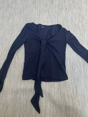 Mörkblå knytblus från Gina Tricot - Snygg mörkblå långärmad topp från Gina Tricot med knyt framtill och v-ringad hals. Tunn och mjuk i materialet, sitter snyggt och har en feminin touch.
