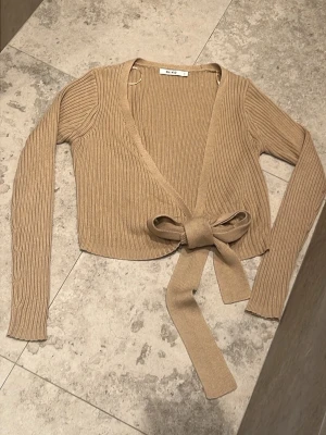 NY Beige omlottkofta från NA-KD - Söt beige omlottkofta från NA-KD med knytband i midjan. Den är tillverkad i ett mjukt, stretchigt material och passar perfekt att styla över ett linne eller topp. Har inte lappen kvar men är oanvänd 💗