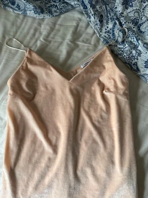 Beige glittrig linnetopp från Gina Tricot - Snygg glittrig beige linnetopp från Gina Tricot med tunna axelband och v-ringad hals. Toppen är ärmlös och har en enkel, stilren design som känns lätt och luftig. Perfekt att styla med jeans eller kjol under varma dagar. 