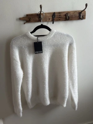 Vit glittrig stickad tröja Pieces - Säljer en vit stickad tröja från Pieces med glittrig effekt. Tröjan har rund halsringning, långa ärmar och är gjord i ett mjukt, fluffigt material som ger en lyxig känsla. Perfekt för dig som vill sticka ut lite extra.