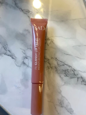 Isadora Glossy Lip Treat nude - Fuktgivande läppglans från Isadora i en snygg nude-rosa nyans. Tuben har en smidig applikator och ger en glansig finish. Perfekt för dig som vill ha återfuktade och glansiga läppar med en naturlig look.