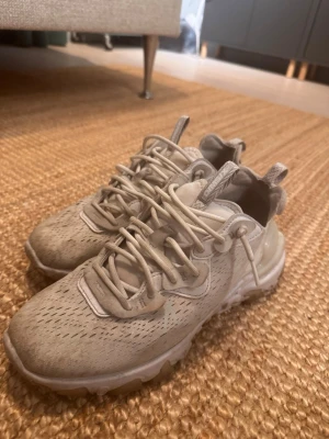 Beige Nike React Element - Snygga  Nike React Element  med unik sula och detaljerade sömmar. Ovandelen är i mesh-liknande material med ventilerande hål och coola snörningar. Perfekta för dig som gillar stilrena och sportiga skor med modern design.