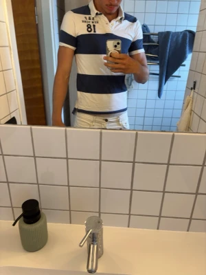 Randig pikéskjorta Abercrombie & Fitch - Säljer en snygg kortärmad pikéskjorta från Abercrombie & Fitch i marinblått och vitt. Skjortan har breda horisontella ränder, klassisk krage och knappar framtill. Perfekt för en avslappnad och sportig look.