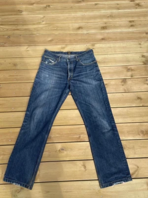 Blå raka jeans från Lee 32/33 - Säljer ett par klassiska blå jeans från Lee med rak passform och fem fickor. Jeansen har en snygg tvättad look.Tillverkade i slitstark denim med gulbruna sömmar och normal midja. Modellen är 180cm/73kg