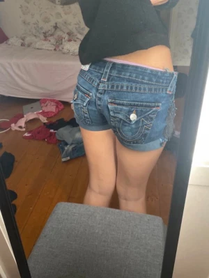 Blå denimshorts från True Religion - Säljer ett par blå denimshorts från true religion. Shortsen har låg midja och en tight passform. Shortsen hadde hål u sig men har sytt ihop och det syns inte i värkligheten kolla sista bilderna. Storlek 24