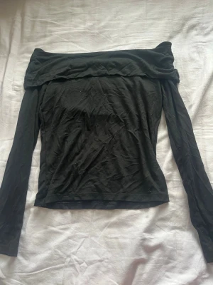 Svart offshoulder topp - Säljer en svart offshoulder topp med långa ärmar. Toppen har en bred kant upptill som ger en snygg och trendig look. Perfekt att styla med jeans eller kjol för en cool outfit.