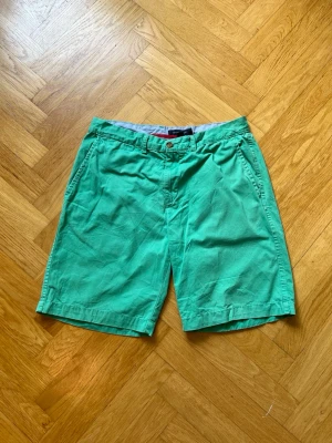 Gröna shorts från Tommy Hilfiger - Snygga gröna shorts från Tommy Hilfiger med klassisk passform och bälteshällor. Shortsen har två sidofickor fram och två bakfickor med knapp. Perfekta för varma dagar och har en fräsch, somrig vibe.