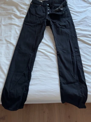 Svarta Levi's 501 jeans - Klassiska svarta Levi's 501 jeans med raka ben och knappgylf. Jeansen har fem fickor och är tillverkade i kraftig denim. Passar perfekt för dig som gillar tidlös och avslappnad stil.