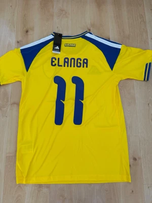 Elanga #11 – Sverige Hemma (storlek M) - Elanga #11-tryck. Sverige Hemma (gul). Storlek M. Helt ny och aldrig använd. Skickas snabbt 🚚💨  Mått (M): Halvt bröstmått 53 cm • Längd 74 cm • Ärmbredd 23 cm • Axelbredd 44 cm • Ärmlängd 40 cm • Manschett 19 cm.  🔥 Fan Edition – normal och bekväm passform. 🇸🇪 Sverige landslag.  📩 Frågor eller prisförslag? 🛍 Bundle-rabatt upp till 20% 💰 📦 Skickas samma eller nästa dag 🌟