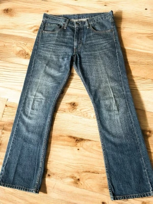 Levi's 527  bootcut raw denim jeans - Klassiska blå jeans från Levi's med bootcut passform och fem fickor. Jeansen har en snygg tvättad look med slitningar och kontrastsömmar. Tillverkade i slitstark denim med den ikoniska läderlappen bak i midjan och röd Levi's-tagg på bakfickan.