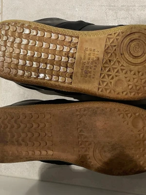Svarta sneakers med gummisula - Svarta sneakers med ovandel i mocka och läder, samt detaljer av färgstänk. Skorna har en klassisk låg siluett och en ljusbrun gummisula med mönster undertill. Insidan är ljusbeige och designen är stilren med en sportig känsla.