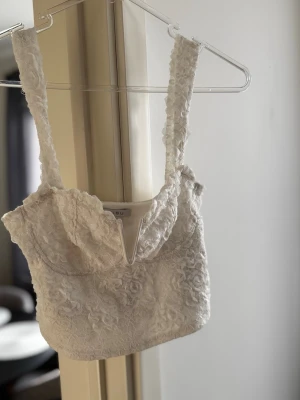 Vit spetslinnetopp  - Supersöt vit linnetopp från AMISU, new yorker. Toppen är täckt av blommig spets och har en croppad passform. Perfekt att styla med jeans eller kjol för en trendig look.
