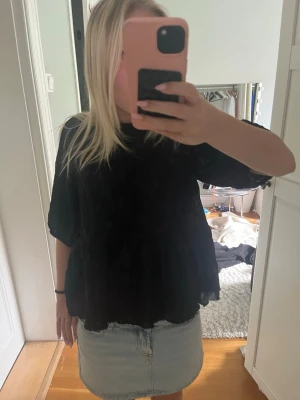 Svart blus med öppen rygg och rosett - Säljer en svart blus med lös passform och halvlånga ärmar. Blusen har en öppen rygg med en söt rosettdetalj upptill. Perfekt för dig som gillar trendiga detaljer och vill ha något extra till garderoben.