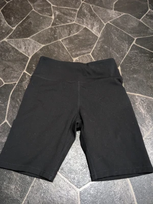 Svarta cykelshorts tights leggings från H&M Sport - Säljer ett par svarta cykelshorts från H&M Sport med hög midja och stretchigt material. Perfekta för träning eller chill dagar. Klassisk modell utan fickor och med bekväm passform.