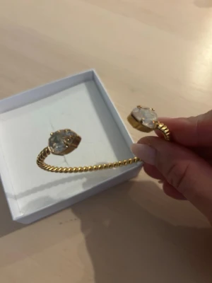 Guldarmband Caroline Svedbom - Snyggt guldpläterat armband från Caroline Svedbom med tvinnad design och två stora, klara kristaller i ändarna. Armbandet är öppet och flexibelt, vilket gör det lätt att ta på och av. Oanvänd present så praktiskt taget som nytt. 