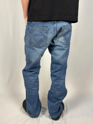 506 Original jeans från Levi's - Klassiska blå jeans från Levi's med rak passform och fem fickor. Jeansen har en ljus tvätt och är tillverkade i slitstark denim. Typisk Levi's-detalj med röd etikett på bakfickan. Perfekta för en avslappnad och tidlös stil | Storleken är 182 cm |