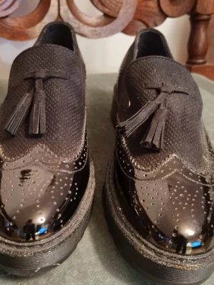 Svarta loafers Anna Field  - Snygga svarta loafers med dekorativa tofsar framtill och broguemönstrad detalj i blankt konstskinn på tån. Ovandelen med små prickar och sulan är kraftig och svart. Perfekta för dig som vill ha en stilren men ändå unik look. Aldrig använda, så i nyskick. 