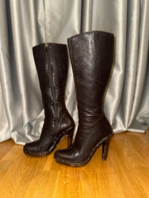 Vintage Gucci Mörkbruna höga läderstövlar med trä klack - Säljer ett par vintage Gucci mörkbruna höga stövlar i äkta läder med rundad tå och trä platform klack. Snygga nitar längs sulkanten och dragkedja på insidan. 