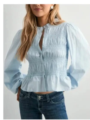 Ljusblå smockad blus med puffärm - Trendig ljusblå blus med smockad front och puffiga långärmar. Blusen har en liten ståkrage och knäppning framtill. Heeelt oanvänd💕