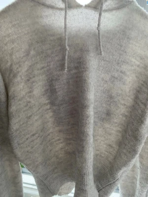 Ljusgrå stickad hoodie - Mysig ljusgrå stickad hoodie med huva och dragsko. Tillverkad i ett mjukt, lätt transparent material som ger en avslappnad och trendig look. Perfekt för dig som gillar en chill och enkel stil.