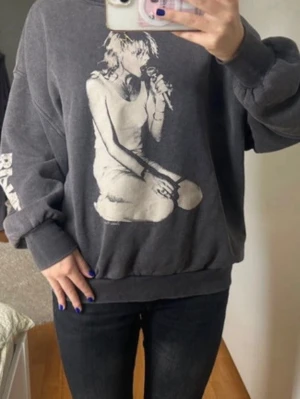 Oversized svart sweatshirt med tryck - Cool oversized svart sweatshirt med stort vitt tryck av en artist som sjunger på framsidan. Tröjan har rund hals, ribbade muddar och tryck på ena ärmen. Perfekt för dig som gillar streetwear och statement-plagg.