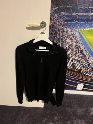 Svart stickad tröja Tiger of Sweden - Jag säljer denna Snygga svarta stickade tröjan från Tiger of Sweden eftersom den var för liten när jag köpte den. Tröjan har halv dragkedja och hög krage. Perfekt för dig som gillar stilrena plagg med enkel design. Tröjan har långa ärmar och är tillverkad i mjukt material som känns skönt mot huden. 