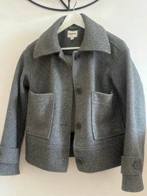 Grå jacka från Kappahl - Stilren grå jacka från Kappahl. Jackan har knäppning med stora knappar framtill och långa ärmar med breda muddar. Perfekt både höst och vår jacka och enkel att matcha till olika outfits.