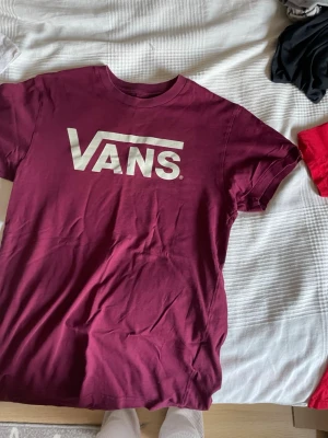 Vinröd Vans t-shirt med logga - Snygg vinröd t-shirt från Vans med stor vit logga på bröstet. Klassisk passform och rund halsringning. Perfekt för dig som gillar streetwear och vill ha en enkel men stilren look.