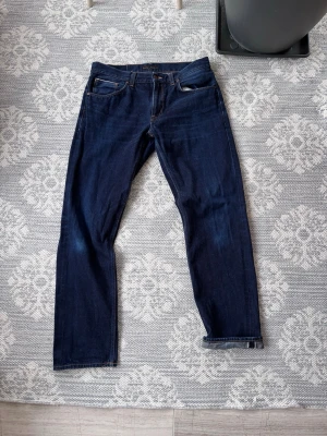 Nudie jeans dry selvage gritty jackson - Nudie jeans dry selvedge jeans i storlek 34/34. Selvage id på fickan ock nere vid benet, dessa kommer att få riktigt coola slitningar när man använder dem.          Snygga mörkblå jeans från Nudie Jeans med klassisk femficksmodell och raka ben. Jeansen har kontrastsömmar och är tillverkade i kraftigt denimtyg. Perfekta för en stilren och avslappnad look.