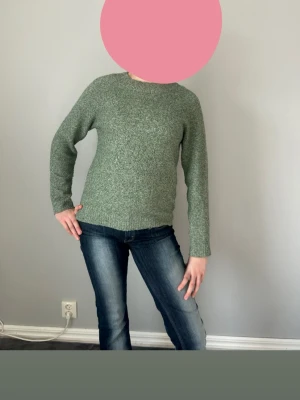 Grönmelerad stickad tröja - En enkel och snygg grönmelerad stickad tröja med rund hals och långa ärmar. Tröjan har en rak passform och ribbstickade muddar vid ärmslut och nederkant. Perfekt för lager på lager och passar till jeans eller kjol.