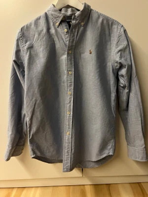Ralph Lauren skjorta - En schysst blå Ralph Lauren skjorta i storlek 16 år, vilket motsvarar ungefär xs/s(160-176 cm.) Perfekt nu till sommaren, hör gärna av dig om frågor finns. Kolla sista bilden, pris kan diskuteras