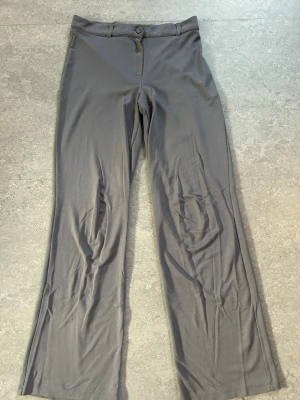 Grå kostymbyxor med raka ben - Snygga grå kostymbyxor med raka ben och klassisk passform. Byxorna har knapp och dragkedja framtill samt bälteshällor i midjan. Materialet ser ut att vara mjukt och stretchigt, perfekt för en clean och stilren look.