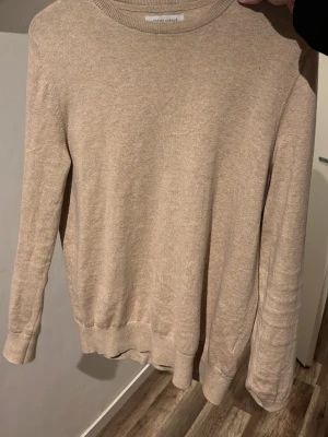 Beige kashmir från Brown Avenue - En stilren beige cashmere tröja från Brown Avenue. Tröjan har rund halsringning, långa ärmar och ribbade muddar vid ärmslut och nederkant. Perfekt basplagg i mjukt material som passar till det mesta.