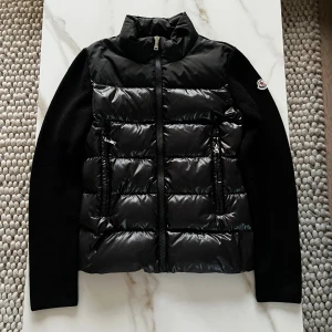 Svart cardigan jacka från Moncler - Säljer en äkta svart cardigan jacka från Moncler med pufferfront och stickade ärmar. Jackan har dragkedja framtill, två sidofickor med dragkedja och Moncler-logga på vänster ärm. Inga defekter och i fantastiskt skick. Modellen är 172cm! Hör av dig vid frågor eller funderingar🙌✅