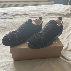 Svarta sneakers med nitar från Christian Louboutin - Säljer ett par svarta sneakers från Christian Louboutin med svarta nitar på tån och längs sidorna. Skorna har snörning och är tillverkade i mocka med läderdetaljer invändigt. Kommer med originalkartong och dustbag, Pris går att diskutera!!