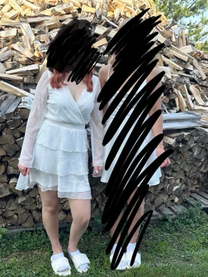 Vit omlottklänning med volang - Söt vit kortklänning med omlottliv och v-ringning. Klänningen har långa, transparenta ärmar och flera lager volang i kjolen. Perfekt studentfirande eller liknande.