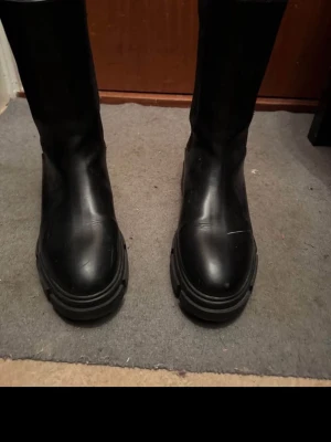 Chunky svarta Chelsea boots - Säljer ett par svarta Chelsea boots med chunky sula och högt skaft. Skorna har elastiska paneler på sidorna och är tillverkade i ett slätt material som liknar läder. Perfekta för dig som vill ha en edgy och trendig look.