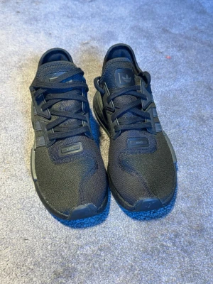 Svarta Adidas NMD sneakers - Snygga helsvarta Adidas NMD sneakers med mesh-överdel och klassiska tre ränder på sidan. Skorna har en låg profil, gummisula med hexagonmönster och diskreta NMD-detaljer på ovandelen. Perfekta för dig som gillar stilrena och sportiga sneakers.