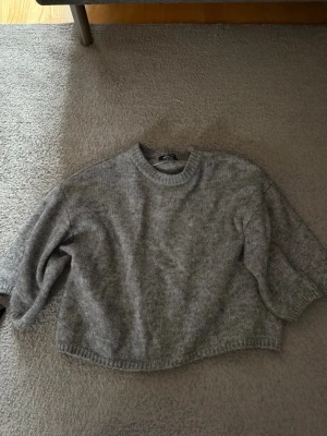 Grå stickad tröja från Gina Tricot - Bra skick. Tröjan ser betydligt mycket större ut på bilderna än vad den ser ut på. Mysig grå stickad tröja från Gina Tricot i storlek XS. Perfekt för lager på lager och enkel att matcha med jeans eller kjol.