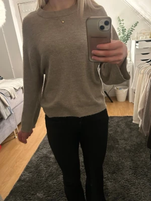 Beige stickad tröja  - Mysig beige stickad tröja med rund halsringning och långa ärmar. Tröjan har en avslappnad passform och ribbstickade muddar vid ärmslut och nederkant. 