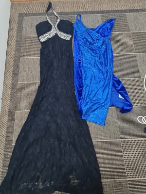 Två långklänningar i svart och blått - Säljer två långklänningar: en svart spetsklänning med halterneck och glittriga detaljer vid halsen, samt en blå glittrig klänning i oneshoulder-modell med paljetter. Perfekta för bal eller festliga tillfällen.