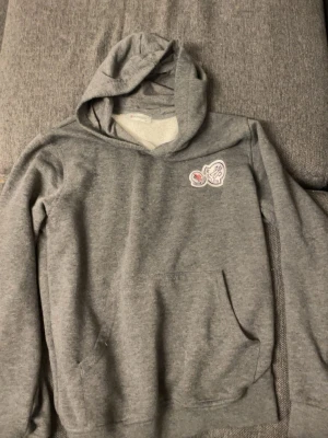 Grå moncler hoodie  - Säljer en grå hoodie från moncler med en cool patchdetalj på bröstet. Hoodien har klassisk känguruficka, huva och ribbade muddar. Mjuk och skön bomullsblandning, perfekt för chill dagar eller när du vill ha en enkel men snygg look.